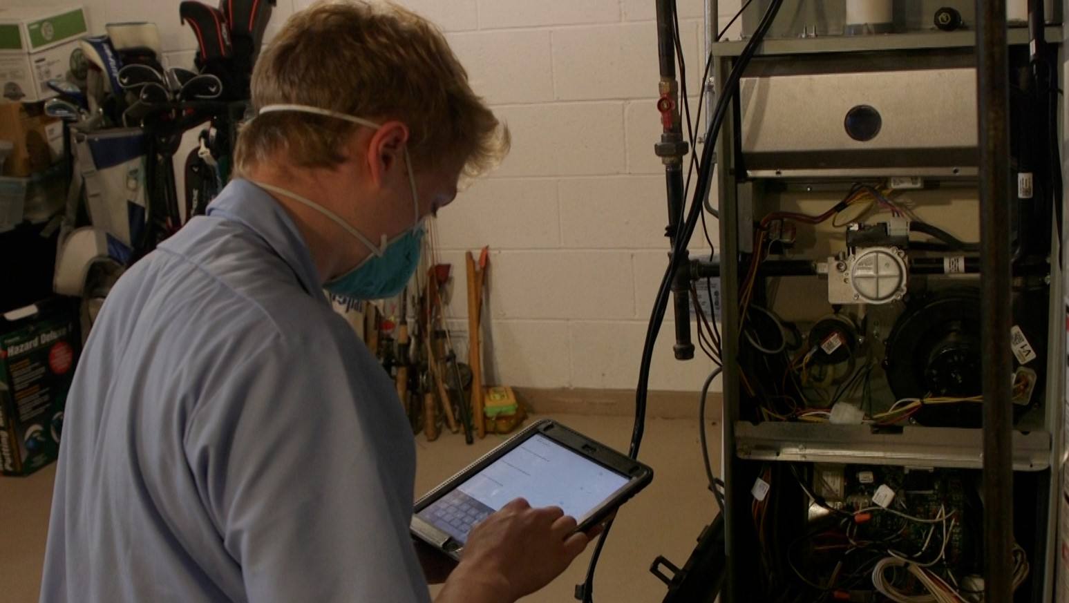 A Fire & Ice service technician kneels in front of a furnace, inputting information on an iPad.