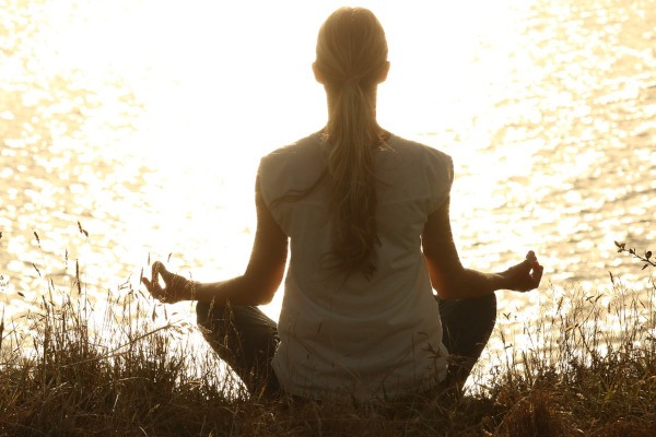 A woman sitting in a lotus position in front of a body of water