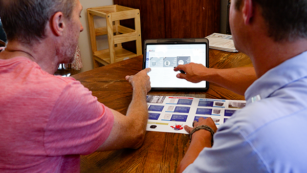 Two men sitting together at a table, interacting with a tablet computer reviewing HVAC options